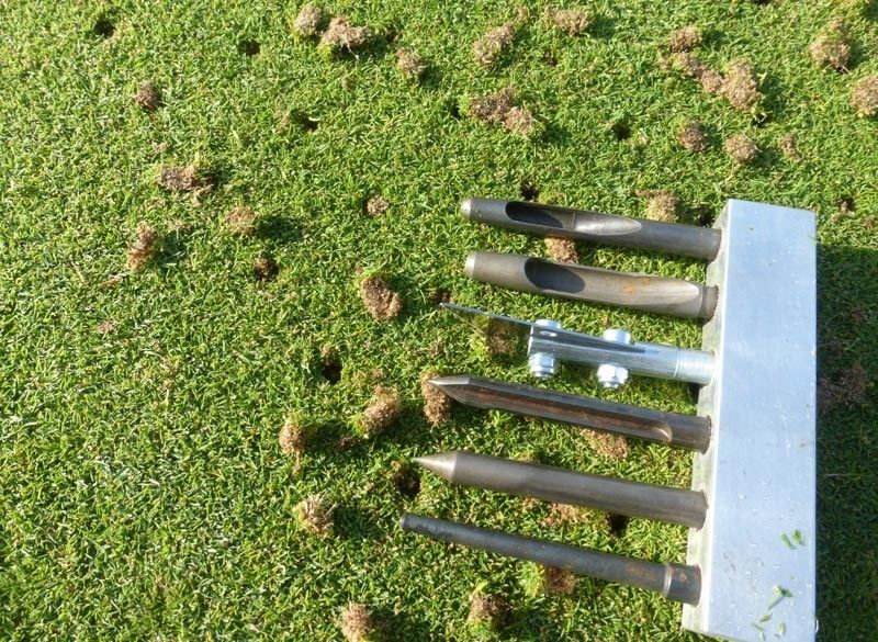 Hollow-tining aerator tool resting on grass with removed soil plugs