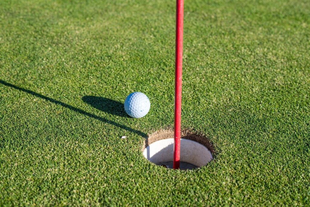 Golf ball beside a red flagstick and hole on a putting green