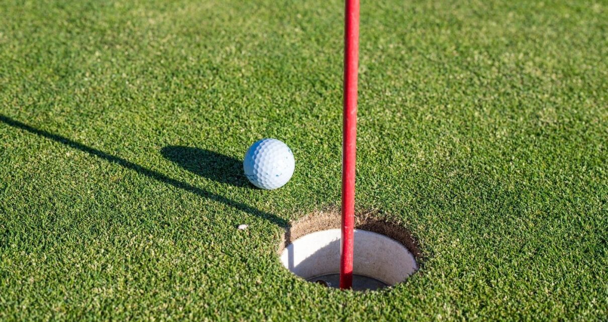 Golf ball beside a red flagstick and hole on a putting green
