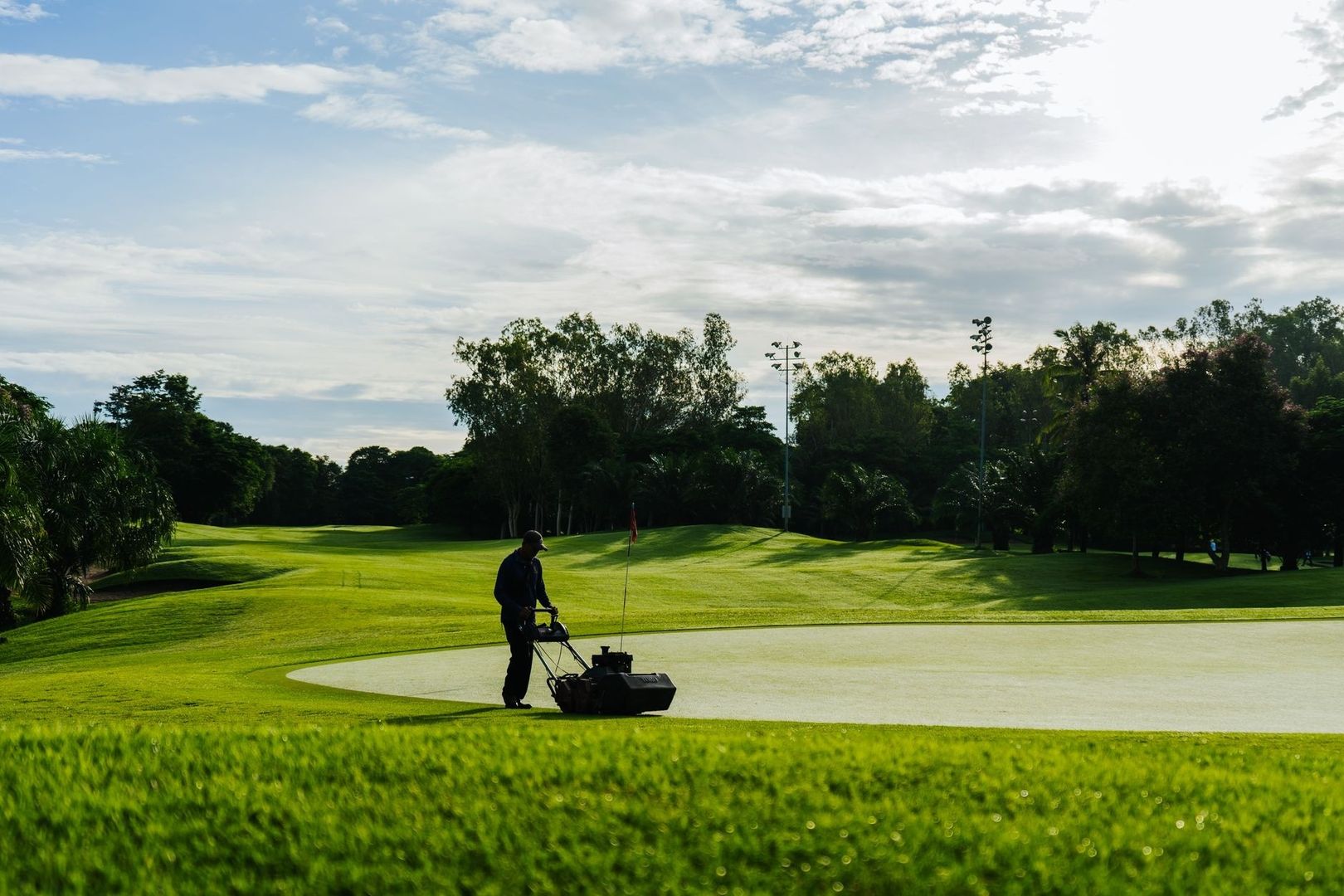 Greenkeeper mowing a golf green beside a red flag