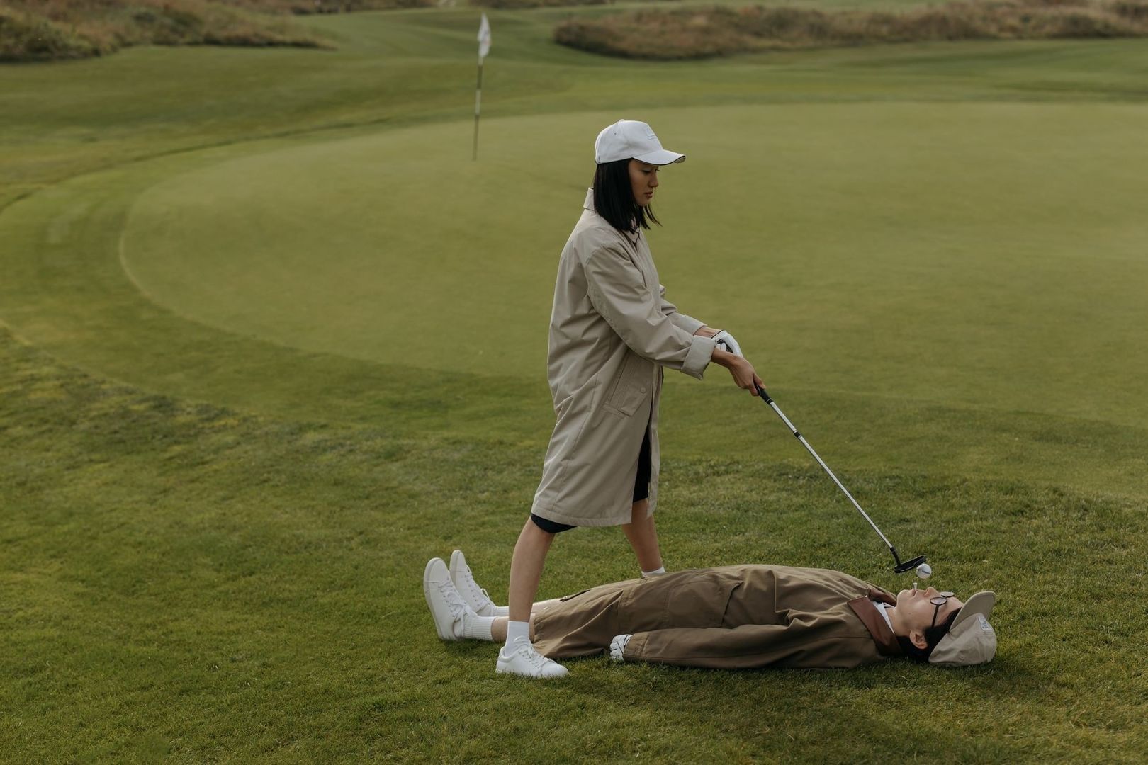 Golfer standing beside a person lying on an undulating green