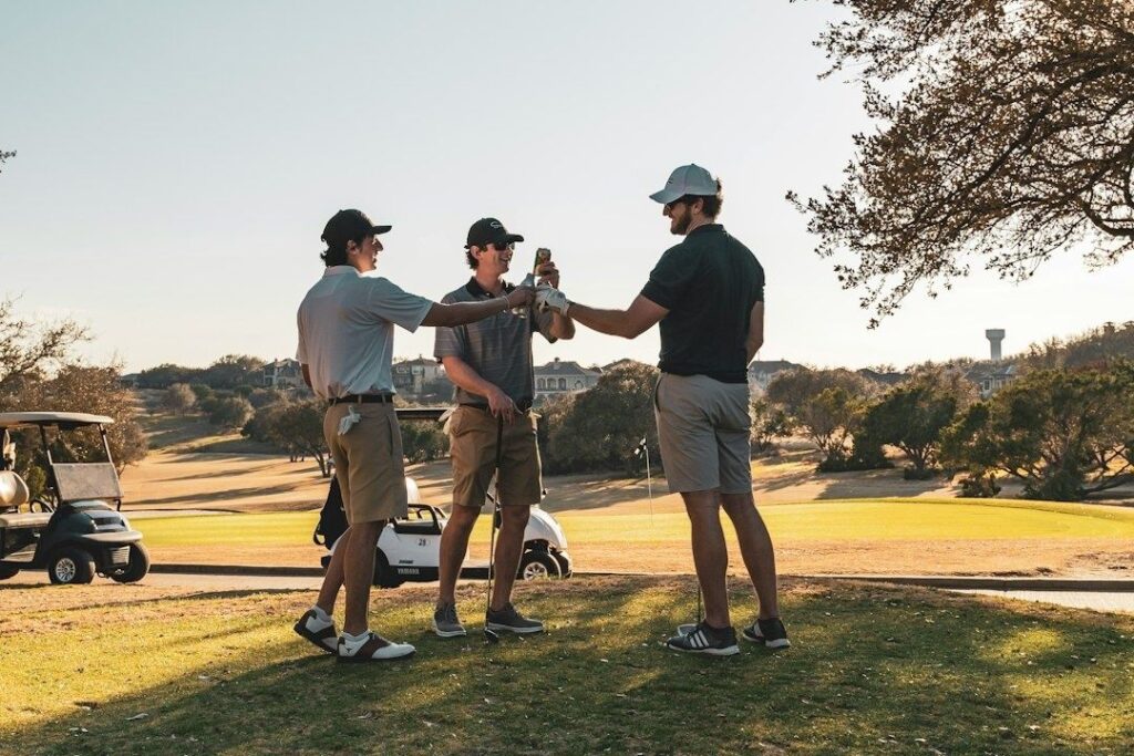 Three golfers clink drinks beside a golf cart on the course